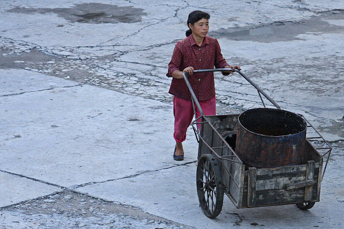  Mulher empurrando um carrinho de mão na Coreia do Norte.