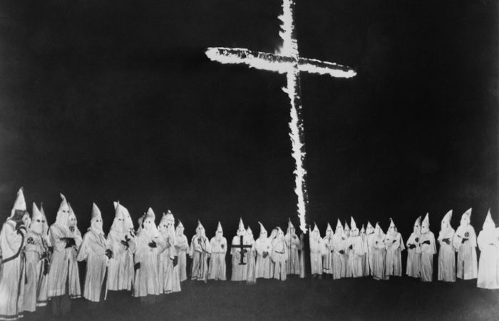 Membros da Ku Klux Klan ao redor de uma cruz em chamas, um dos símbolos da organização.
