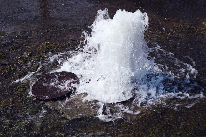 Água jorrando de um poço de visita como representação do desperdício de água.