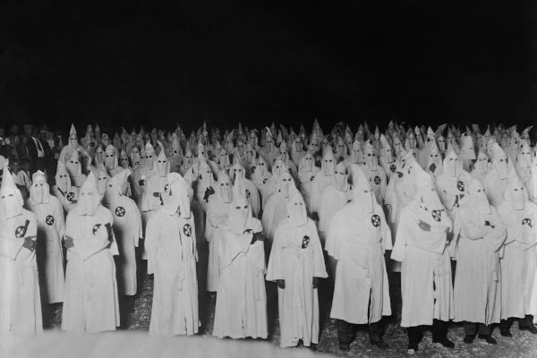 Membros da Ku Klux Klan vestidos de branco e com capuz em formato cônico, também branco, sobre o rosto.