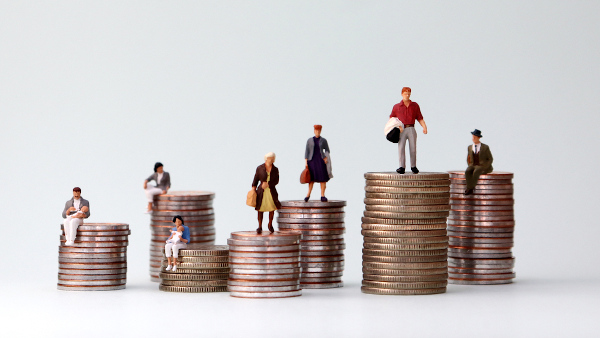 Miniaturas de pessoas em cima de pilhas de moedas, representando a renda nacional.