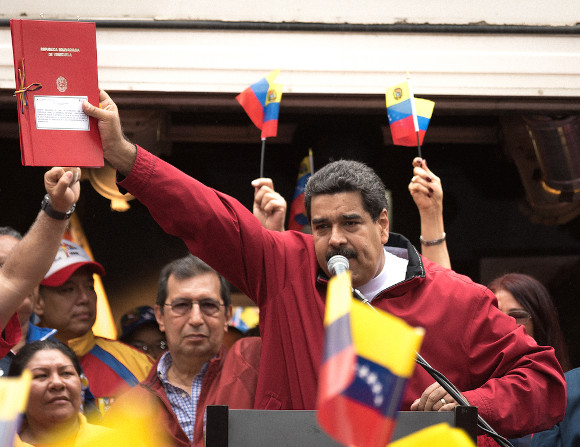 Nicolás Maduro discursando em palanque e erguendo, com a mão direita, uma pasta vermelha.