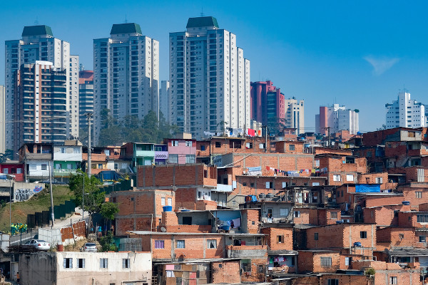 Paisagem contrastante com grandes edifícios atrás de favelas, exemplo de segregação socioespacial.