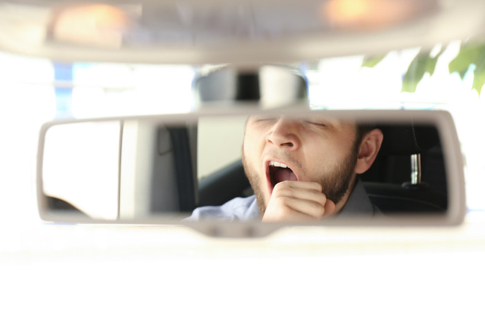 Reflexo de um homem bocejando no espelho do retrovisor de um carro; sono excessivo é um sintoma de narcolepsia.