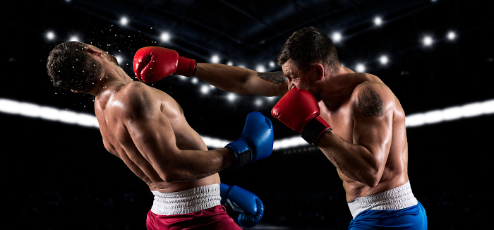 Atleta com luva vermelha realiza golpe em atleta com luva azul em uma luta de boxe, uma das principais artes marciais.