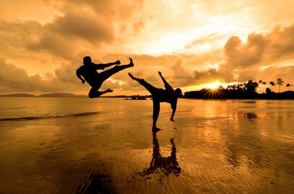Duas pessoas em movimento de luta em uma praia como representação das artes marciais.