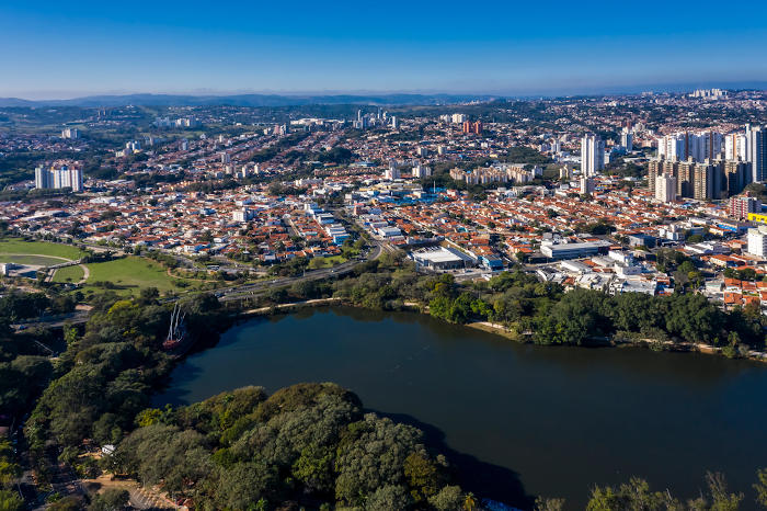 Vista aérea de Campinas, metrópole brasileira, com um grande lago próximo à paisagem urbana.