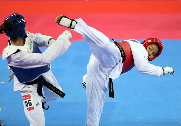 Atleta realizando chute na oponente durante uma competição de taekwondo, uma das principais artes marciais.
