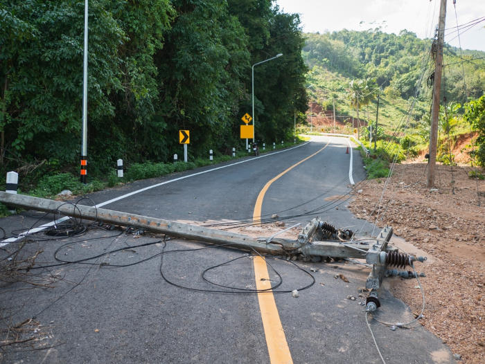 Poste de energia caído em uma rua asfaltada como exemplo de uma das causas de um apagão.