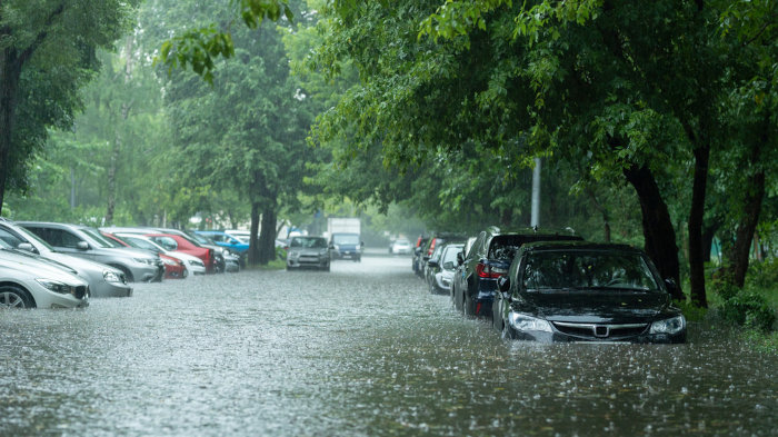Carros cercados por água da chuva em região urbana atingida por enchente.