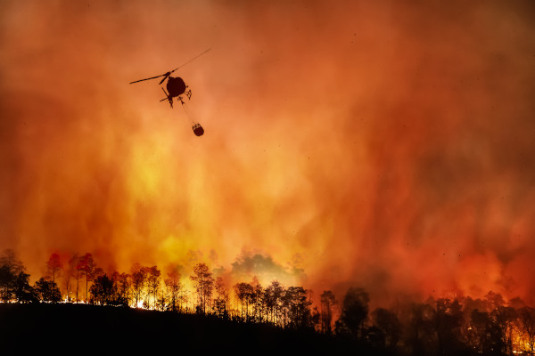 Helicóptero carregando um grande recipiente com água para ajudar a apagar um incêndio florestal.