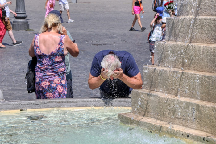 Homem idoso lava o rosto em fonte de água para aliviar-se do calor intenso da cidade.