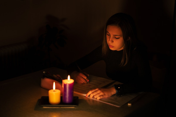 Jovem estudando à luz de velas como consequência de um apagão.