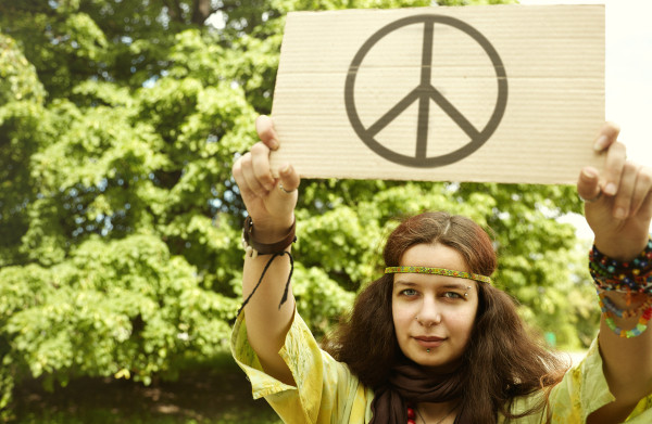 Mulher segurando um pedaço de papelão com o símbolo adotado pelo movimento hippie na década de 1960.