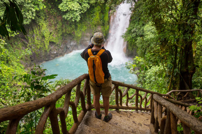 Homem fotografando a queda d’água de uma cachoeira na Costa Rica.
