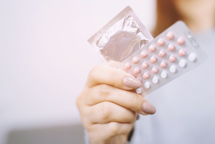 Mulher segurando dois contraceptivos, instrumentos usados para planejamento familiar, que se opõe ao controle de natalidade.