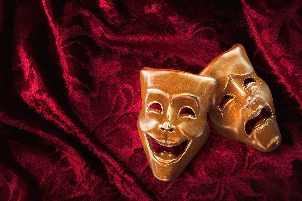 Máscaras da tragédia e comédia, componentes do gênero dramático, sobre tecido vermelho.