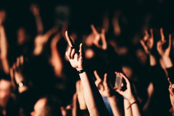 Pessoas na plateia de um show fazendo o símbolo do rock com as mãos.