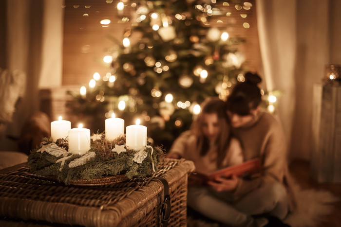 Mãe e filha lendo um livro próximo à Coroa do Advento, uma guirlanda com quatro velas, um importante símbolo do Natal.