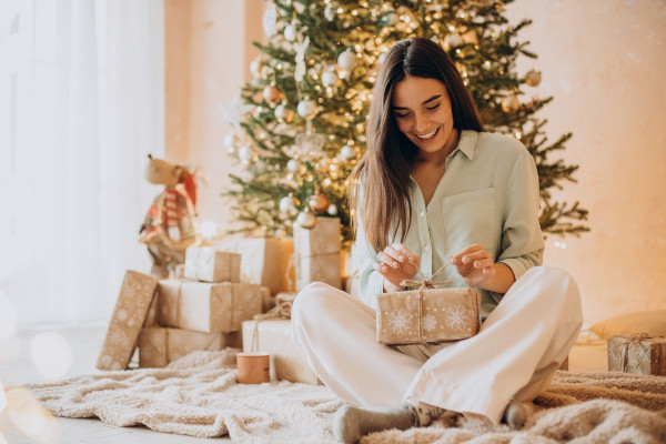 Mulher abrindo um dos presentes de Natal que recebeu, prática natalina cuja origem é desconhecida.