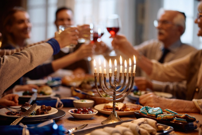 Menorá acesa em uma mesa com comidas e judeus brindando na festa do Hanukkah.