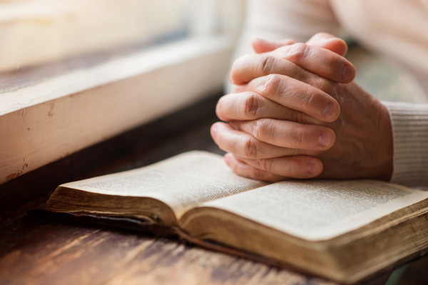 Mãos em posição de oração em cima de Bíblia.
