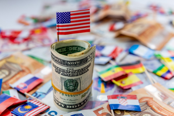 Notas de dólar americano, com a bandeira dos Estados Unidos, perto da bandeira de vários países como exemplo de hegemonia.