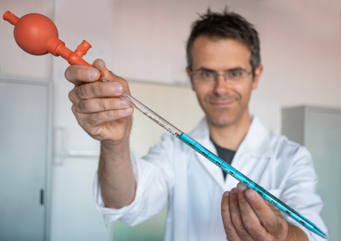 Cientista segurando uma pipeta com pera de sucção, parte das vidrarias de laboratório de Química.