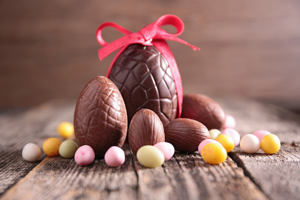 Ovos de chocolate, símbolo da Páscoa, em superfície de madeira e rodeados de pequenos ovos coloridos.