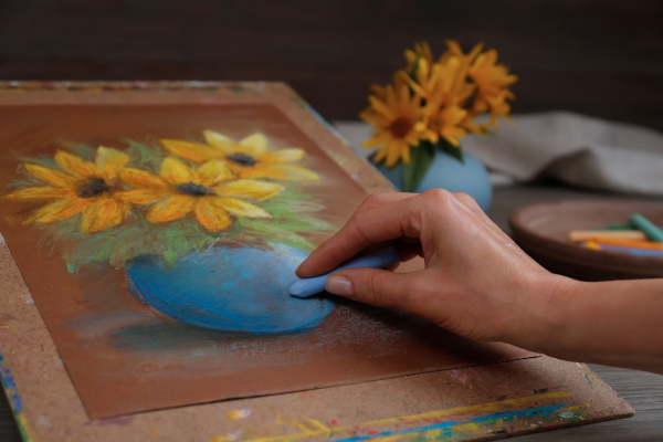 Pessoa pintando um vaso de flores com giz, uma alusão à força de atrito. Título: forca-atrito