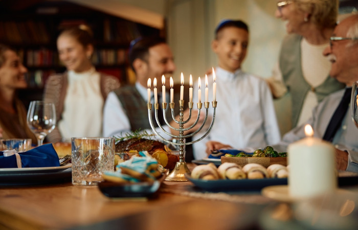 Família reunida em volta de mesa com comida e um chanukiá, símbolo do judaísmo, em primeiro plano.