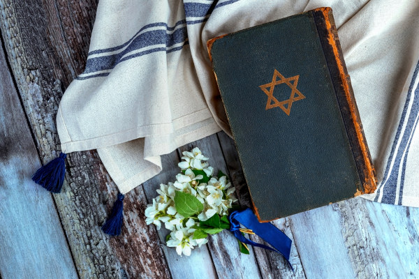 Talmude, livro do judaísmo, com um ramo de flores ao lado, em superfície de madeira.