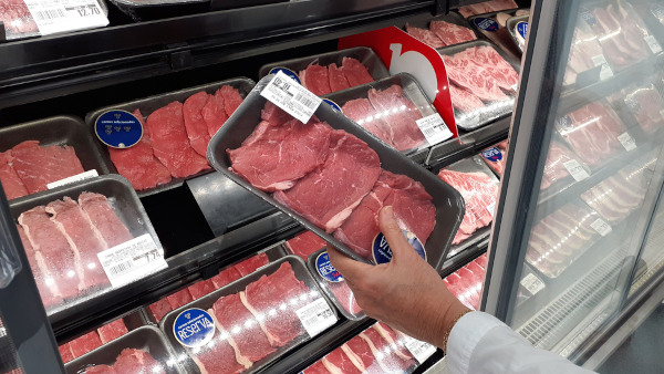 Pessoa escolhendo bandeja de carne em supermercado, em texto sobre consumo de carne e aquecimento global.