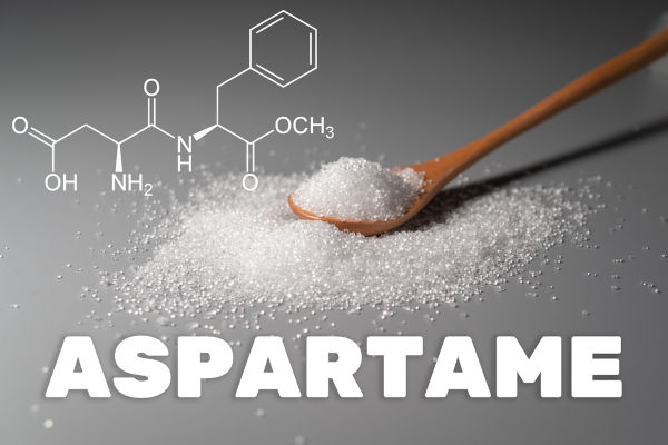 Colher de madeira com aspartame entre a estrutura química do aspartame e o escrito “aspartame”.