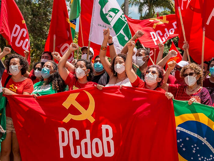 Apoiadores do PCdoB erguendo bandeiras do partido de extrema-esquerda durante passeata.