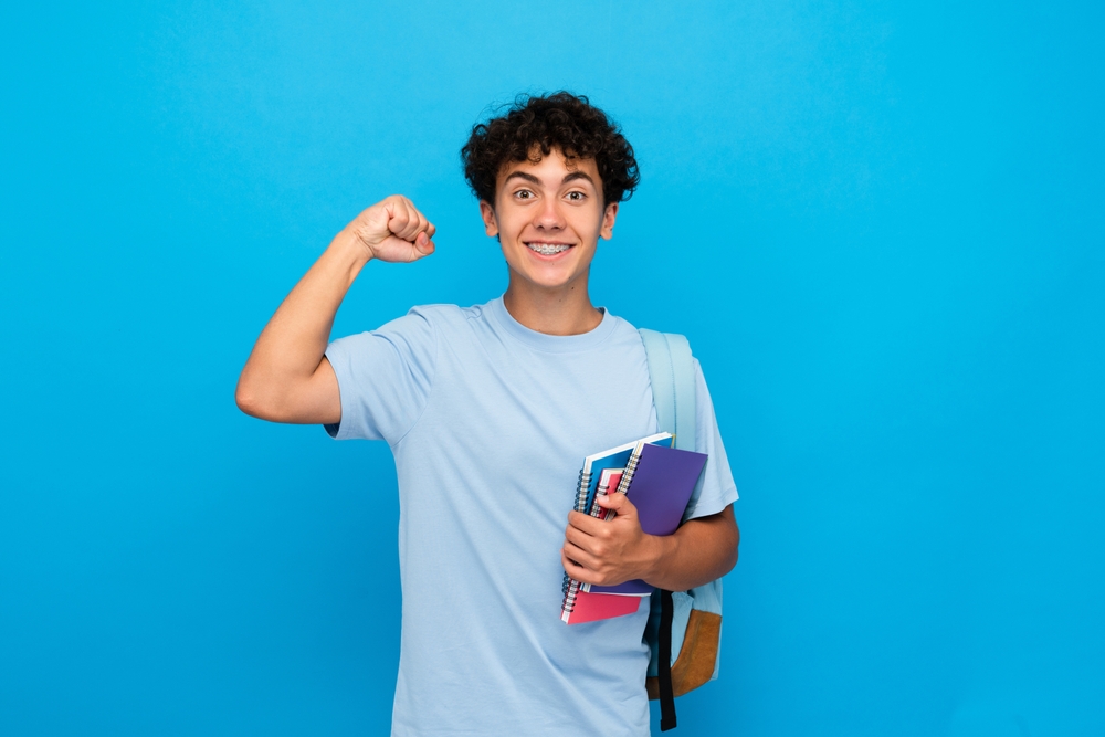 estudante com aparelho sorrindo e com o braço levantado comemorando