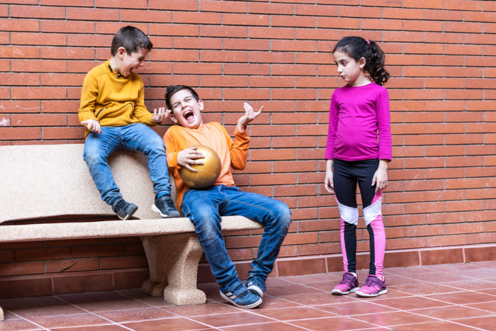 Dois meninos rindo de uma menina, situação ligada ao aspecto do machismo de superioridade masculina e inferioridade feminina.