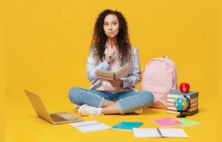 Jovem sentada de pernas cruzadas rodeada de livros e com o notebook na frente