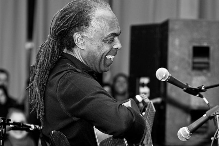 Gilberto Gil sorrindo em uma performance musical.