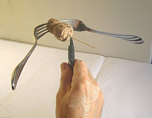 Pessoa equilibrando uma rolha de vinho com dois garfos e um palito na ponta de uma caneta. Pessoa equilibrando uma rolha de vinho com dois garfos e um palito na ponta de uma caneta.