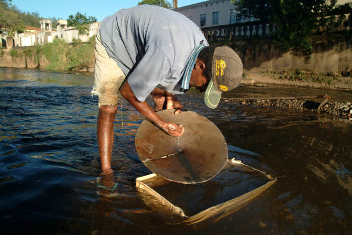 Mulher segurando recipiente com papéis, separados pelo método da catação para reciclagem.Garimpeiro separando minérios com um prato de metal, pelo método da levigação.
