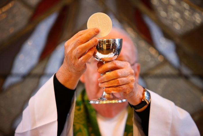 Padre levante hóstia e cálice, durante a eucaristia, que é celebrada no Corpus Christi.