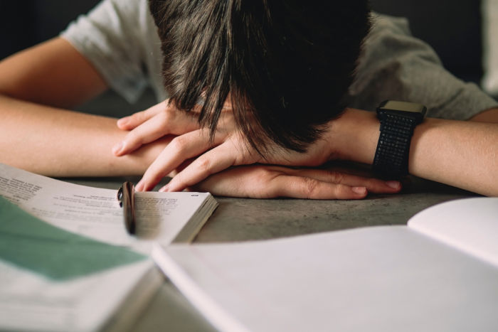Jovem com a cabeça debruçada sobre livros, em alusão às consequências do analfabetismo funcional.