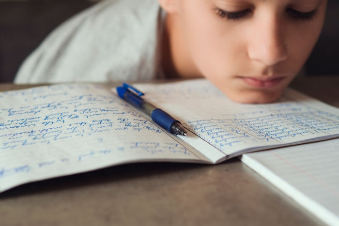 Menino com a cabeça apoiada sobre caderno, em alusão ao analfabetismo funcional.