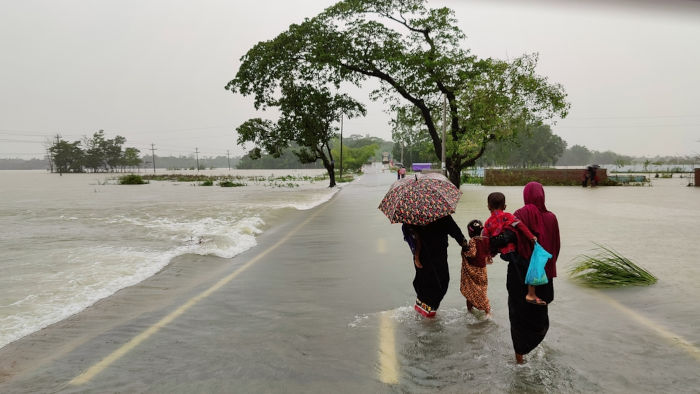 Pessoas caminhando em ruas alagadas por chuvas, resultado das mudanças climáticas, um tema da COP 30.