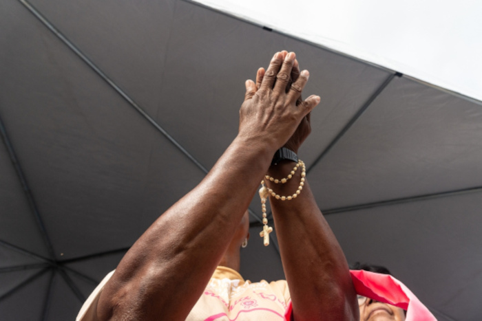 Mãos de uma mulher fazendo prece com um terço, um hábito da cultura brasileira.