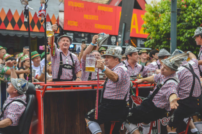 Homens desfilando com copos de cerveja durante o Oktoberfest, festa cultural brasileira. Farinha de mandioca em um tacho, alimento de influência indígena na cultura brasileira.