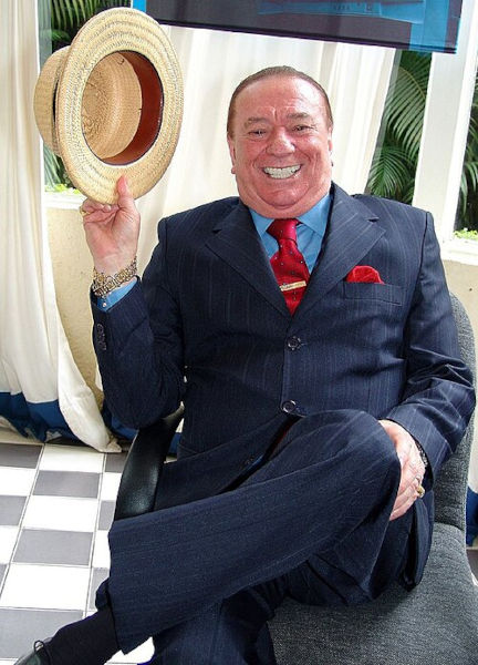 Fotografia de Raul Gil, um dos maiores apresentadores da TV brasileira, sorrindo e segurando chap&eacute;u. [imagem_principal]