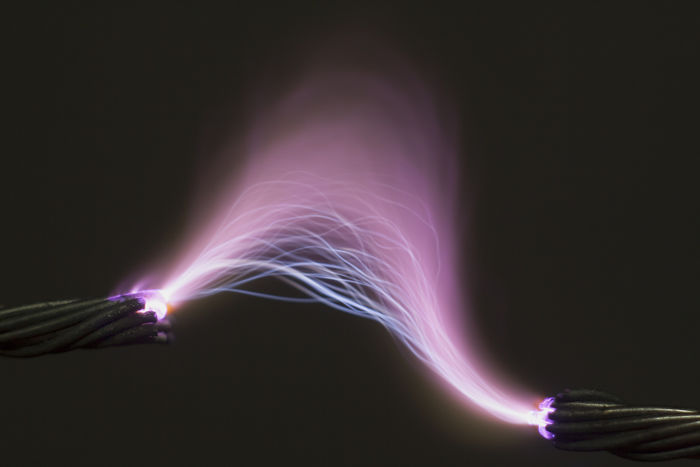 O intenso campo elétrico entre os fios excita o ar ao seu redor, ionizando-o e fazendo com que ele emita luz violeta.