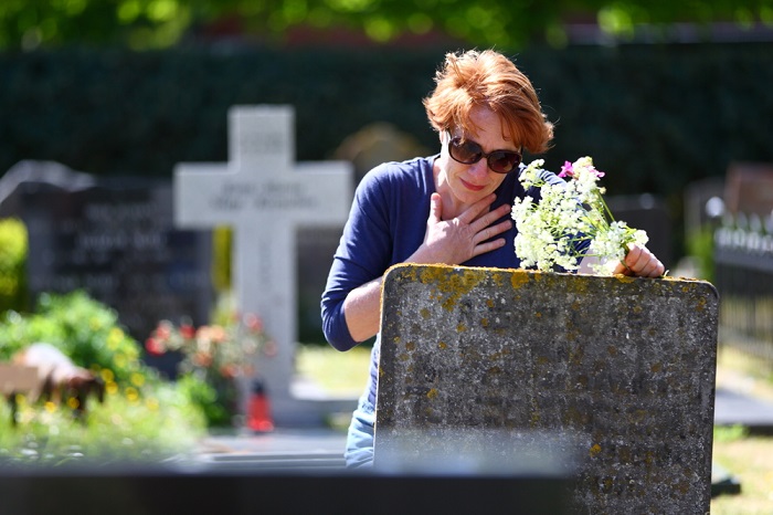 Mulher triste com flores na mão em frente a uma lapide em um cemitério